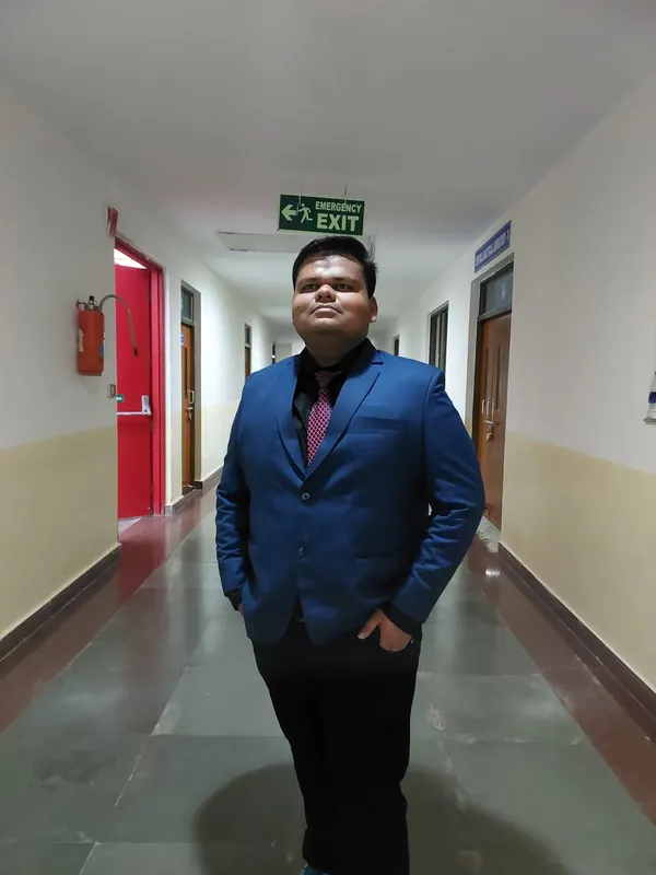 Aditya in a blue suit standing at the centre of a long corridor